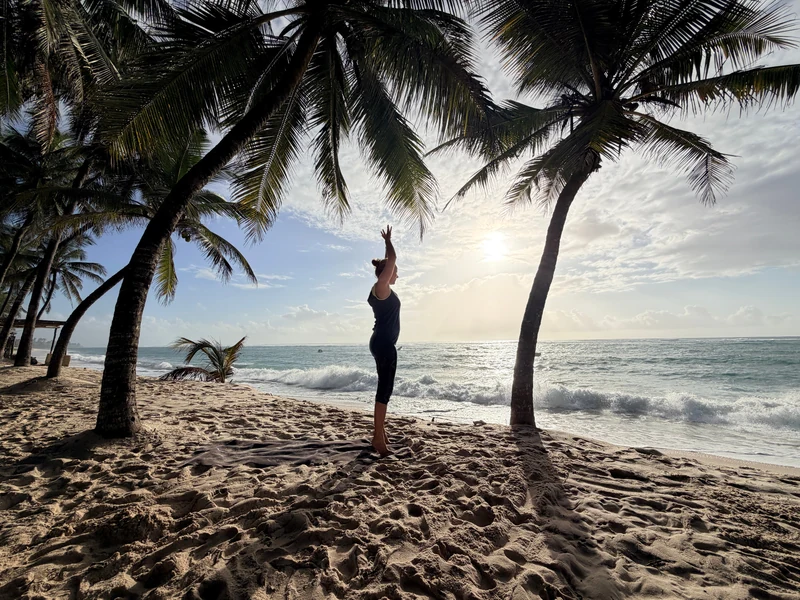 Aufrechte Yogahaltung mit erhobenen Armen am Strand zwischen Palmen