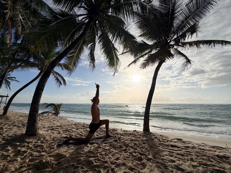 Yoga im knienden Ausfallschritt mit erhobenen Armen unter Palmen am Meer
